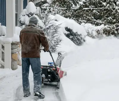 Residential snow removal technician using a snow blower to clear a home driveway and walkway in {city}, {state}